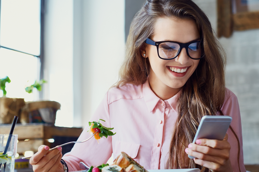 Woman with glasses eating lunch and earning money online playing mobile games